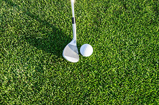 Aerial view of pitching wedge hitting golf ball on a green.