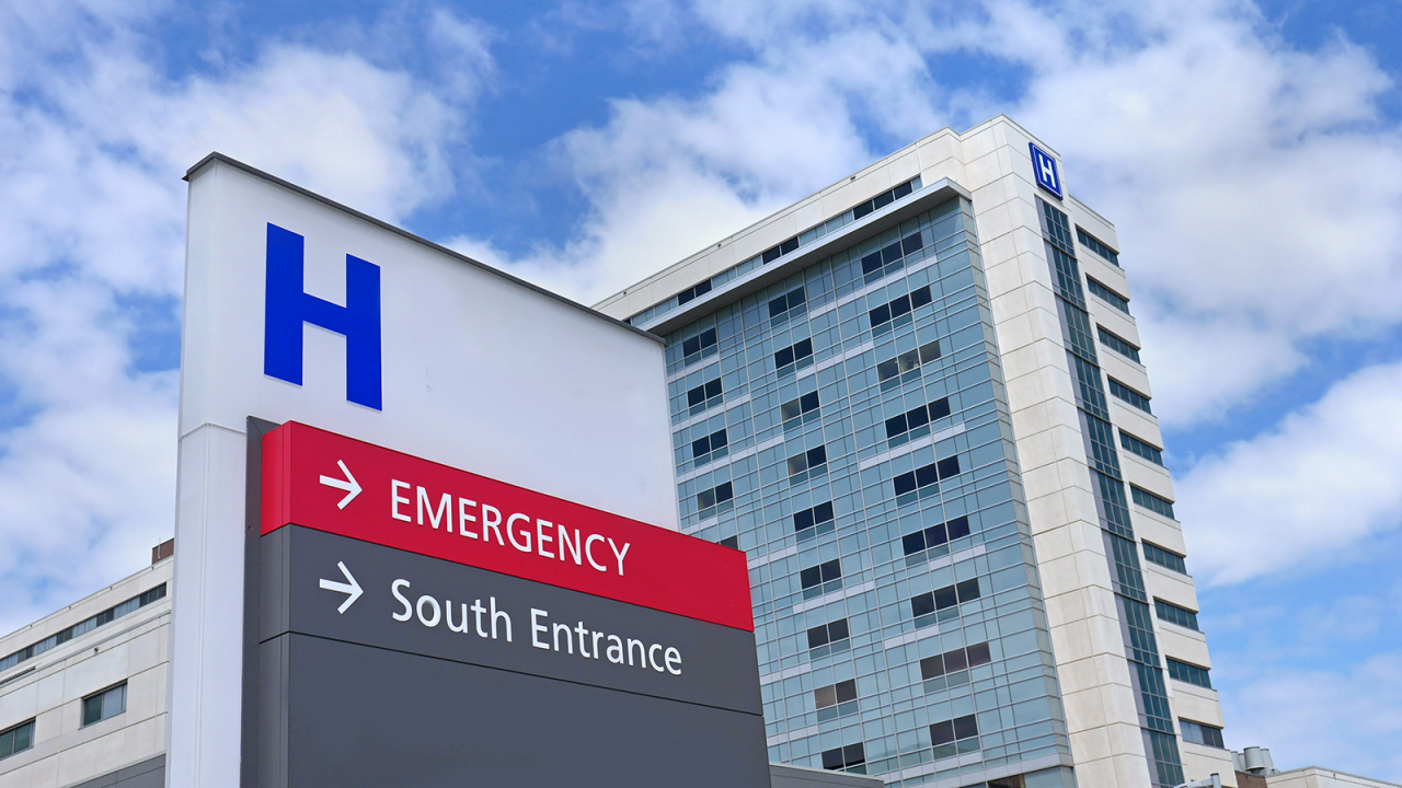 Direction sign for emergency room and south campus for a hospital with the hospital in the background.