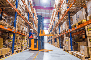 Worker using forklift platform machine to move boxes in a warehouse.