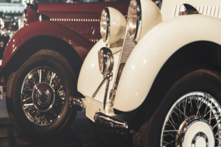 Closeup of the fronts of a red and a white antique car.