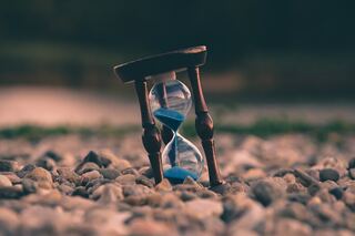 Hourglass timer with blue sand resting on rocks.