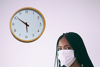 Woman in a mask next to a clock with the time at 5:50