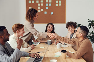 A smiling marketing team in a meeting to brainstorm for a campaign with two members shaking hands.