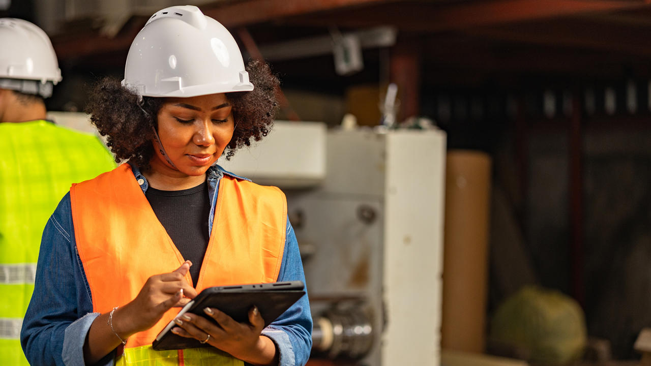 Female engineer wearing safety helmet and vest using MSS on her tablet to analyze the reliability of her products. 