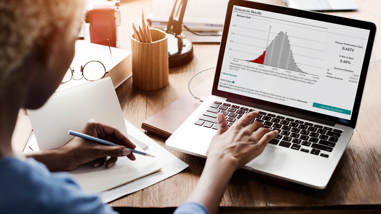 Business woman taking notes on a cluttered desk with a monte carlo simulation on her laptop.
