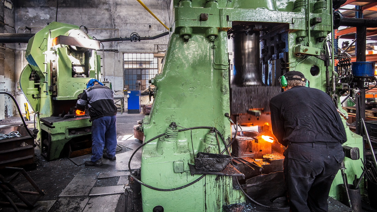 Forging shop with hydraulic hammer shaping red-hot billet to reduce waste.