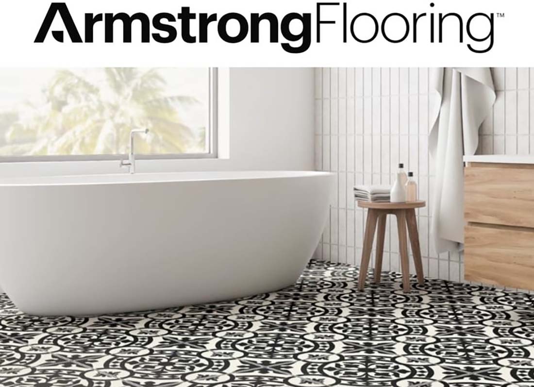 Modern bathroom with bathtub, stool, and vanity and black and white decorative tiles below Armstrong Flooring logo.