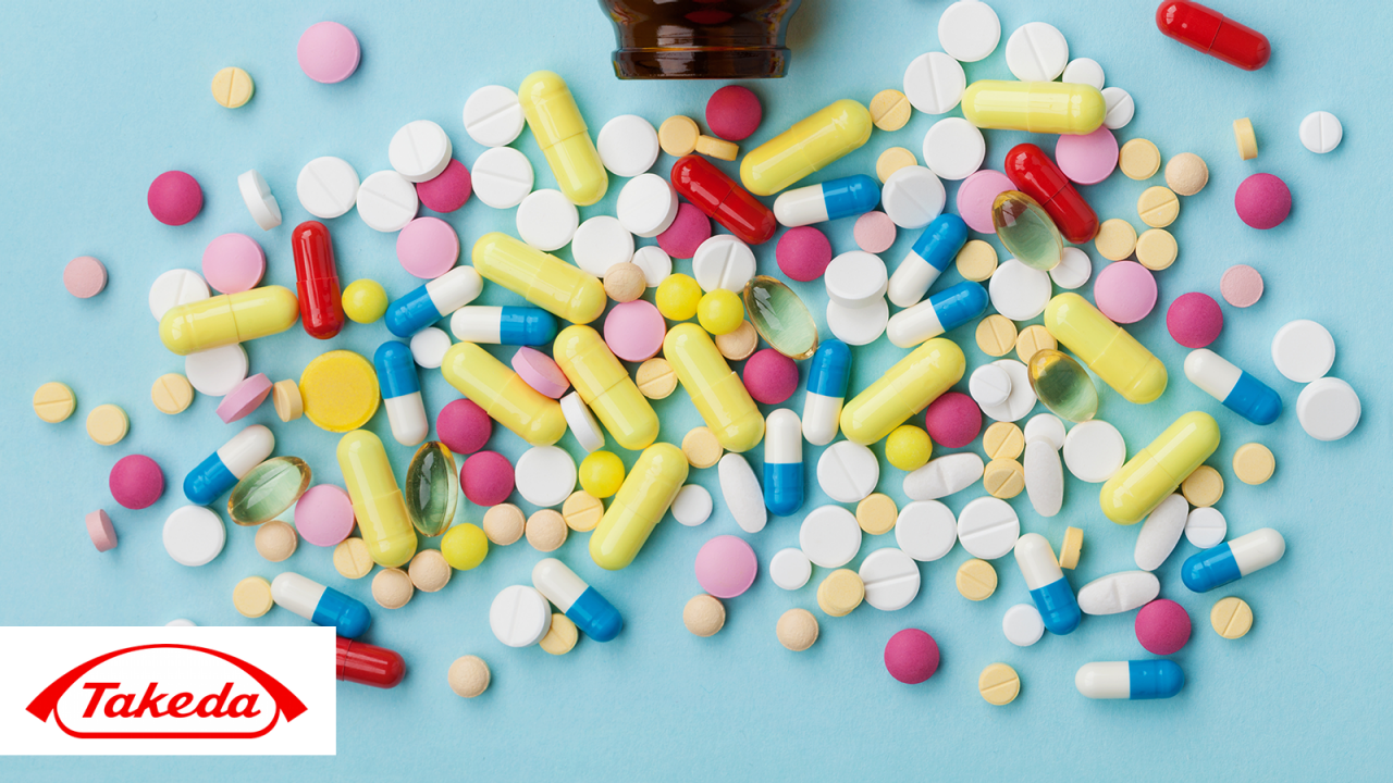 Pile of colorful drug pills of different sizes on a blue background with Takeda logo in corner.