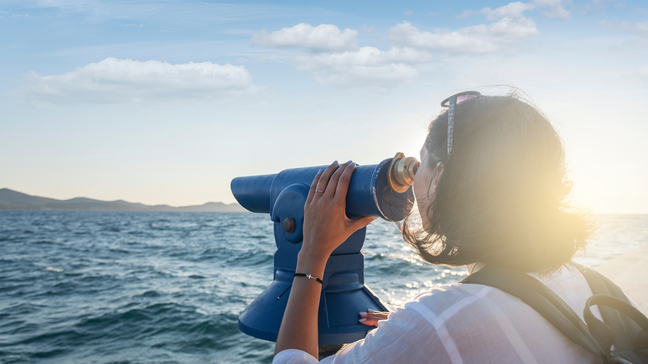 Young woman looks in a telescope or binoculars by the sea.