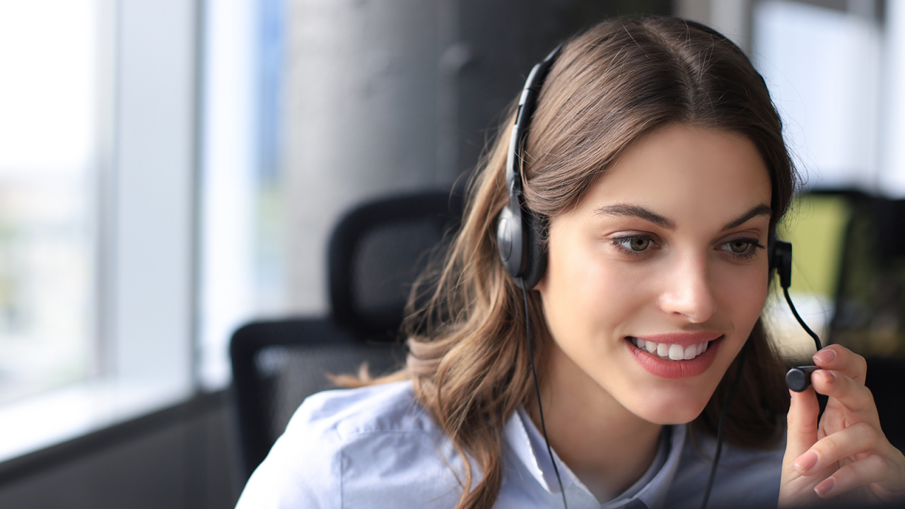 Successful, smiling call center worker with headset working at modern office.