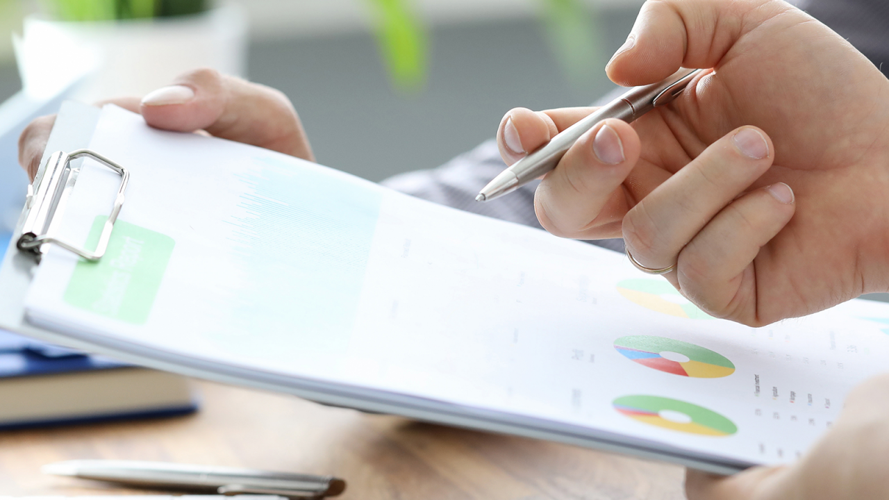 Empresarios con bolígrafo y portapapeles revisan las herramientas de analítica de calidad.