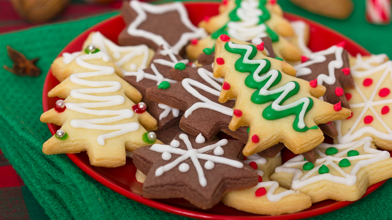 Plato rojo lleno de galletas navideñas decoradas sobre un mantel de mesa verde.