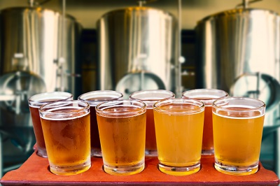 Beer flight of eight glasses of craft beer on a serving board with fermenting tanks background.