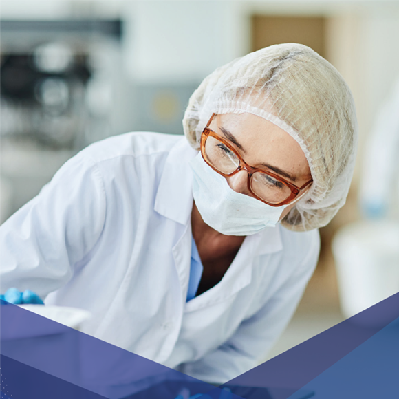 Técnico de laboratório usando máscara, touca e óculos, trabalhando em um ambiente clínico ou estéril.