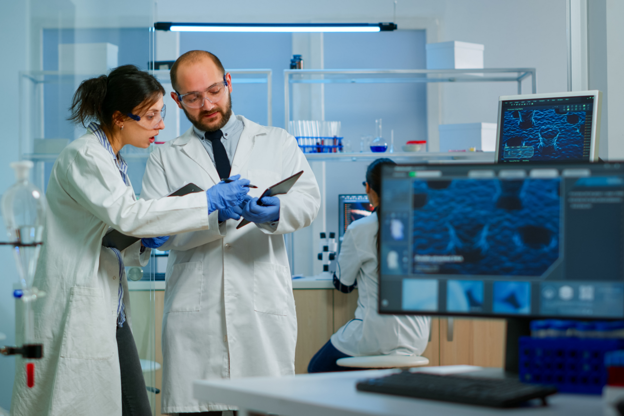 Laboratório de Pesquisa Médica Moderno: Dois cientistas trabalhando, usando um tablet digital, analisando um teste, conversando. Laboratório farmacêutico científico avançado para medicina e desenvolvimento de biotecnologia.