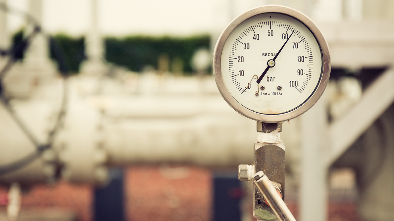Closeup of a high pressure manometer, measuring natural gas pressure. Pipes and valves in the background. Selective focus