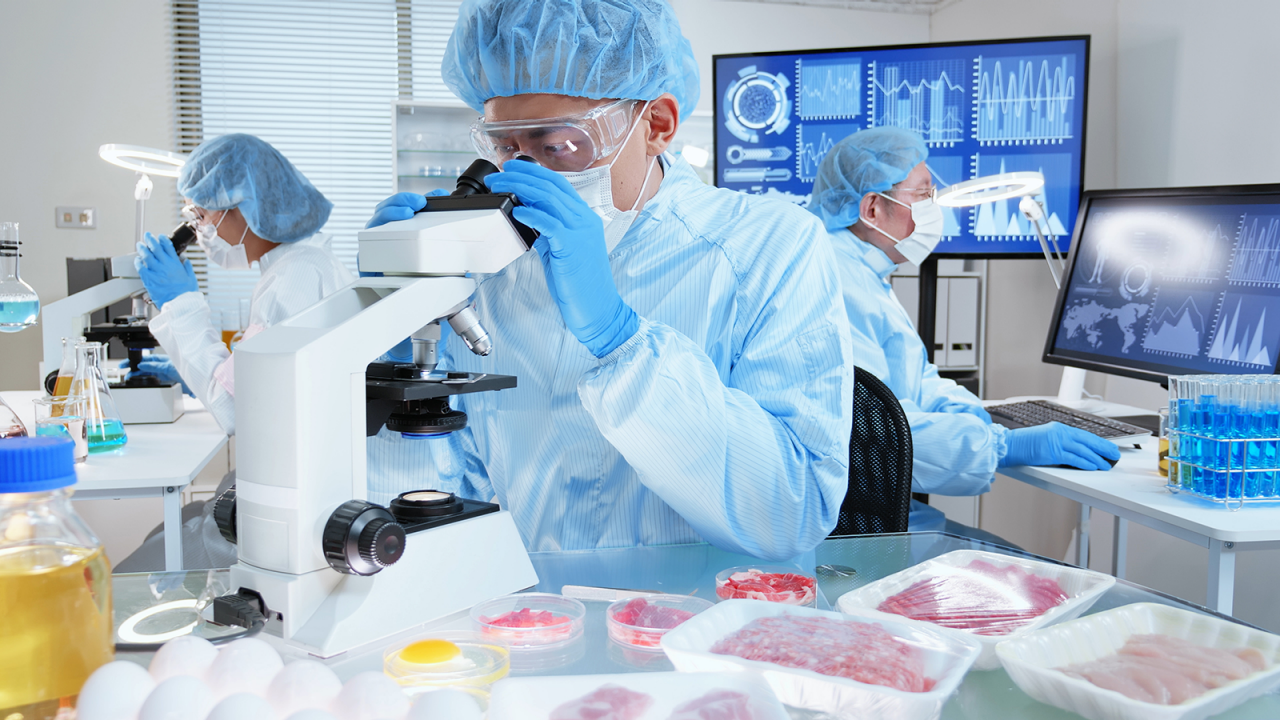 三位科学家在食品实验室用显微镜和电脑软件检测食品污染和食品安全。